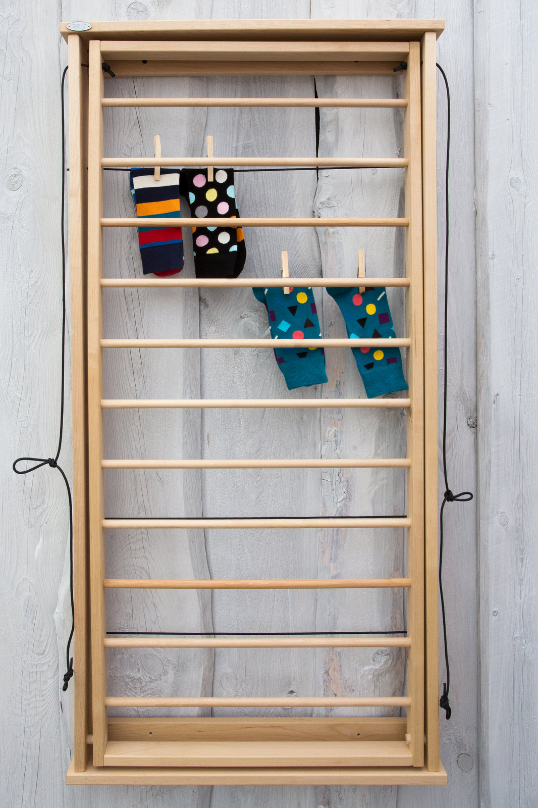 A wooden wall-mounted laundry ladder with clothes hanging on it, against a white background.